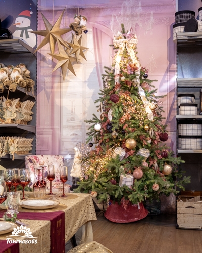 Sapin de Noël décoré de boules roses, dorées et noires, avec étoiles suspendues et table dressée en jardinerie Tournesols